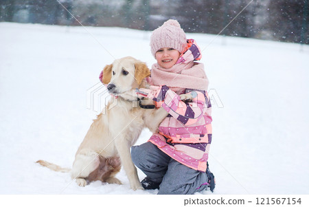 Little Girl Hugging A Golden Retriever Puppy In The Snow Outdoors In Winter 121567154