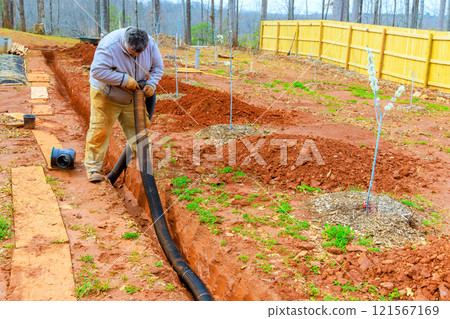 Worker installs drainage pipes in backyard to ensure proper water management for enhance water flow management 121567169