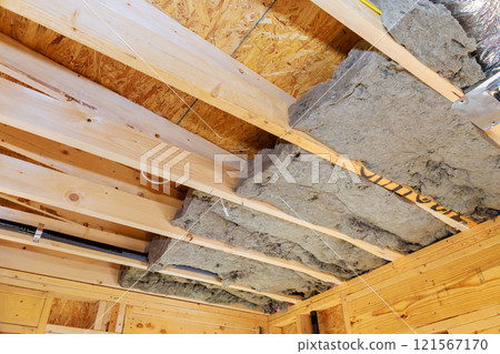 Laying insulation between wooden beams during construction new home at construction site Laying insulation between wooden beams during construction new home at construction site 121567170