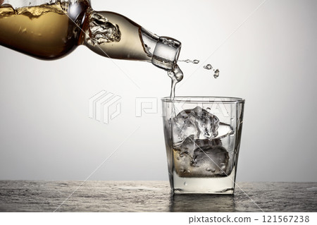 Whiskey is poured from a bottle into a glass with ice. 121567238