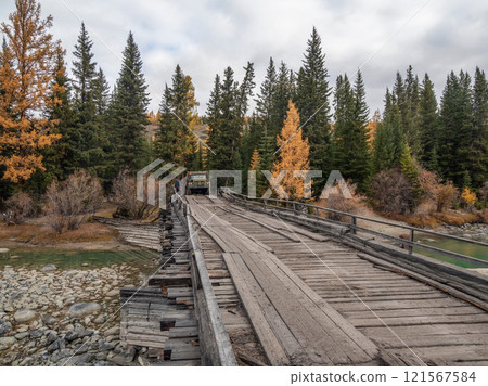 Old truck driving on a dilapidated bridge over a river. 121567584