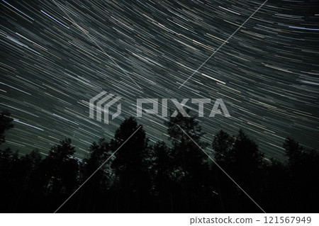 Star trails illuminate a clear night sky over a forested landscape in autumn 121567949