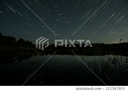 Star trails illuminate a serene lake surrounded by trees at night 121567953