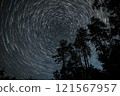 Star trails over a forest at night create a mesmerizing celestial display amidst towering trees 121567957