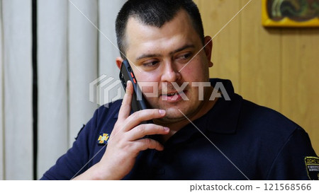 Male firefighter chief have serious telephone conversation with his subordinate by smartphone at fire station. Nervous fireman talking by mobile phone at fire department. Concept of heroic profession 121568566