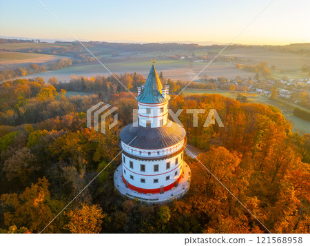 The Baroque Humprecht hunting chateau sits majestically above Sobotka, surrounded by vibrant autumn foliage as the sun rises, casting a golden glow on the landscape. 121568958