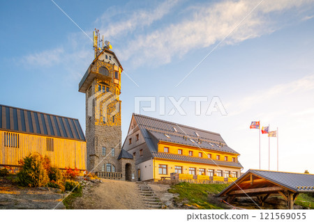 Kralovka Lookout Tower stands tall against a clear blue sky on an autumn morning. The warm sunlight highlights the surrounding landscape in the Jizera Mountains of Czechia. 121569055