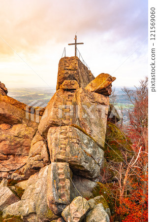 A breathtaking sunset illuminates the Oresnik granite rock formation near Hejnice, showcasing a wooden summit cross and a panoramic lookout point amidst the Jizera Mountains. 121569060