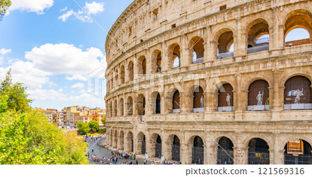 The majestic Colosseum stands prominently under a bright sky in Rome. Visitors admire its architecture, while trees and bustling city life create a vibrant atmosphere. The majestic Colosseum stands prominently under a bright sky in Rome. Visitors admire its architecture, while trees and bustling city life create a vibrant atmosphere. 121569316