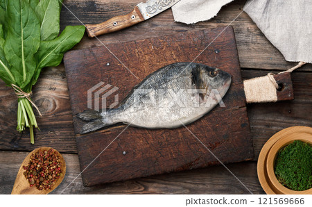 A raw whole dorado fish on a wooden cutting board background, top view 121569666