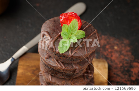 Chocolate brownies stacked, with the top adorned by a juicy red cherry and mint leaves Chocolate brownies stacked, with the top adorned by a juicy red cherry and mint leaves 121569696