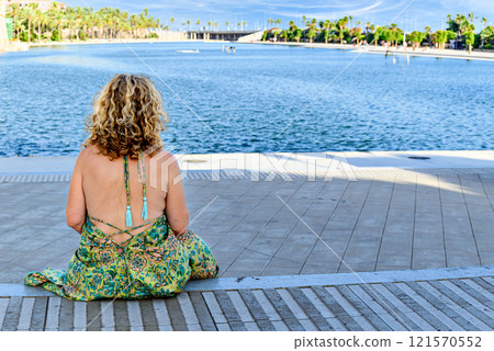Blonde woman with curly hair, sitting looking at the horizon in the Parque del Mar in Mallorca, Balearic Islands, Spain Blonde woman with curly hair, sitting looking at the horizon in the Parque del Mar in Mallorca, Balearic Islands, Spain 121570552