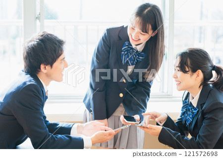 Male and female high school students talking while looking at their classmates and smartphones in the classroom Male and female high school students talking while looking at their classmates and smartphones in the classroom 121572698