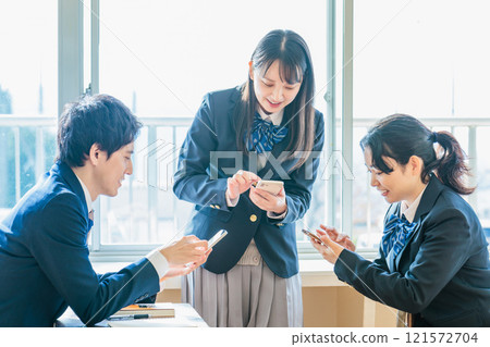Male and female high school students talking while looking at their classmates and smartphones in the classroom 121572704