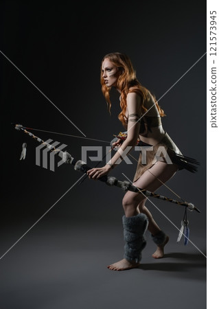Woman dressed in survival attire poses with a bow in a studio setting 121573945