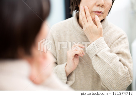 Middle-aged to senior women doing skin care while looking at the bathroom mirror Middle-aged to senior women doing skin care while looking at the bathroom mirror 121574712