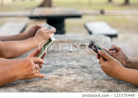 Three people hands holding smartphones over rough stone table in outdoor setting, focusing on technology and connectivity in casual environment 121575449