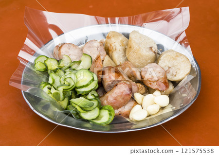 Close-up of Taiwanese sausage and sticky rice (glutinous rice) sausage on a plate, with some garlic and cucumber. This is one of the street snacks popular among tourists in Taiwan. 121575538