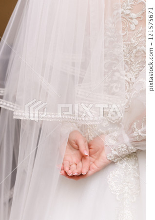 The bride in a wedding dress with a veil folded her hands behind her back The bride in a wedding dress with a veil folded her hands behind her back 121575671