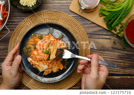 Hands holding fork and plate of freshly prepared kimchi, ready to be enjoyed on rustic wooden table Hands holding fork and plate of freshly prepared kimchi, ready to be enjoyed on rustic wooden table 121575710