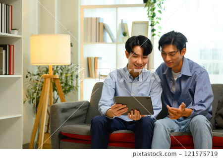 Attractive gay couple relaxing together in living room. LGBT, love and lifestyle relationship concept Attractive gay couple relaxing together in living room. LGBT, love and lifestyle relationship concept 121575719