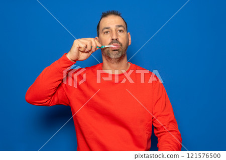 Bearded hispanic man in his 40s brushing his teeth with a toothbrush and toothpaste, cleaning teeth and tongue as a healthy morning health care routine. Bearded hispanic man in his 40s brushing his teeth with a toothbrush and toothpaste, cleaning teeth and tongue as a healthy morning health care routine. 121576500
