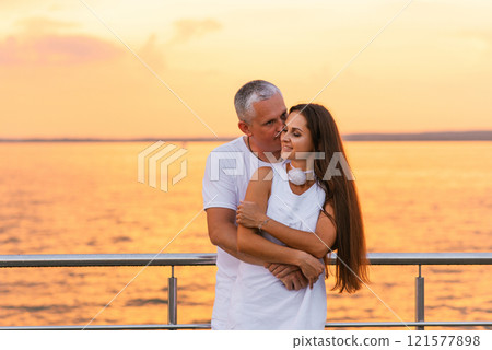 Happy couple is hugging on pier by the water. Young woman has long hair and the man is kissing her. Scene is romantic and peaceful Happy couple is hugging on pier by the water. Young woman has long hair and the man is kissing her. Scene is romantic and peaceful 121577898