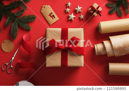 Preparing for the holidays, wrapping gifts. Craft brown wrapping paper, red velvet ribbon, labels, spruce sprigs and ready wrapped gift. 121580993