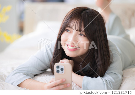 A young woman lying on the bed and looking up with her smartphone 121581715
