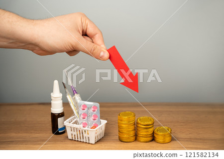 Down arrow, coins and basket with medical pills. Concept of reducing the price of medicines and drugs. Healthcare and medicine. Male hand 121582134