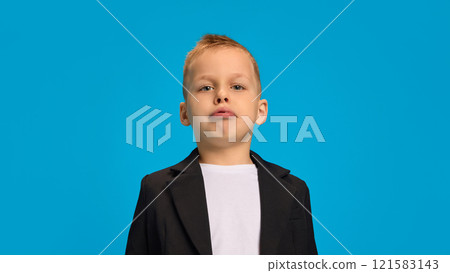 Young boy in black blazer, white shirt, making pouty face while standing upright against bright blue background. Young boy in black blazer, white shirt, making pouty face while standing upright against bright blue background. 121583143