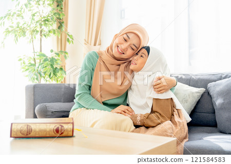 Asian muslim mother sit on sofa beside of her daughter and hug her child they also smiling in concept of happiness muslim family at home. Asian muslim mother sit on sofa beside of her daughter and hug her child they also smiling in concept of happiness muslim family at home. 121584583