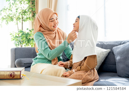 Side view of Asian muslim mother sit on sofa and grab daughter chin also look her child face and they also smiling in concept of happiness muslim family at home. Side view of Asian muslim mother sit on sofa and grab daughter chin also look her child face and they also smiling in concept of happiness muslim family at home. 121584584