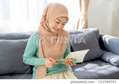 Asian beautiful muslim woman sit on sofa in her house and read the book relate to her religion and smile with happiness. 121584591
