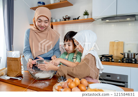 Little boy and girl of muslim family help and learn from their mother to cook relate to cooking flour and ingredients in the kitchen with happiness. Little boy and girl of muslim family help and learn from their mother to cook relate to cooking flour and ingredients in the kitchen with happiness. 121584631