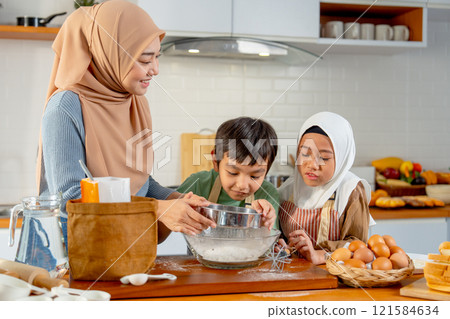 Little boy and girl of muslim family help and learn from their mother to cook relate to cooking flour and ingredients in the kitchen with happiness. Little boy and girl of muslim family help and learn from their mother to cook relate to cooking flour and ingredients in the kitchen with happiness. 121584634
