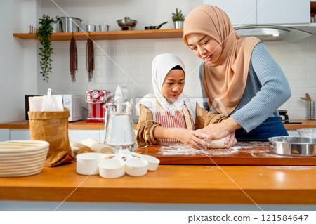 Young Asian muslim mother help and teach her daughter to threshing flour by hands on wooden tray for making the bakery in the kitchen of their house. Young Asian muslim mother help and teach her daughter to threshing flour by hands on wooden tray for making the bakery in the kitchen of their house. 121584647