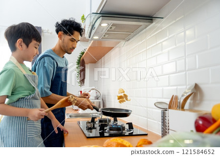 Young Asian father show skill of cooking by throwing pan cake up and his son cheer up beside in the kitchen of their house. 121584652
