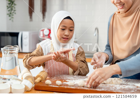 Asian muslim girl enjoy to threshing flour to be like ball shape for making bakery with mother in kitchen of their house. Asian muslim girl enjoy to threshing flour to be like ball shape for making bakery with mother in kitchen of their house. 121584659