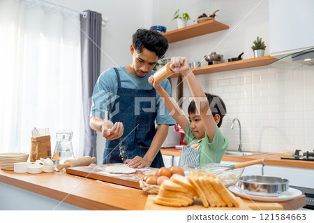 Young Asian father pour cooking flour on wooden tray during teaching his son who hold rolling pin for threshing flour for making bakery in kitchen of their house. Young Asian father pour cooking flour on wooden tray during teaching his son who hold rolling pin for threshing flour for making bakery in kitchen of their house. 121584663