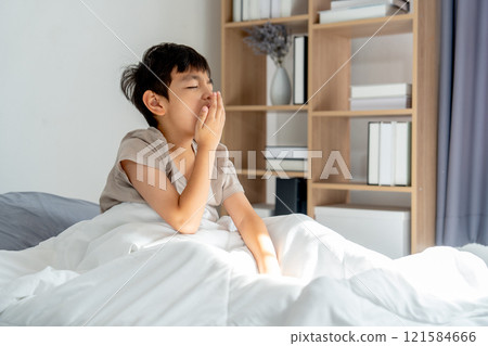 Asian boy sit on bed after wake up in the morning and yawn to express asleep and feel tired. Asian boy sit on bed after wake up in the morning and yawn to express asleep and feel tired. 121584666