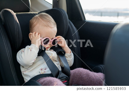 Adorable baby with pink sunglasses in car seat. Concept of safe travel and playful style for little ones 121585933