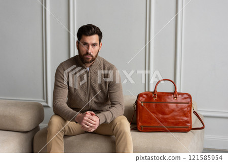 A man is comfortably sitting on a sofa, with a leather orange briefcase A man is comfortably sitting on a sofa, with a leather orange briefcase 121585954