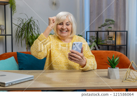Senior grandmother woman at home use smartphone celebrating success victory winning play online game 121586064