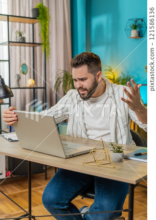 Displeased sad businessman using laptop loss game fail computer virus error bad news at home office 121586136