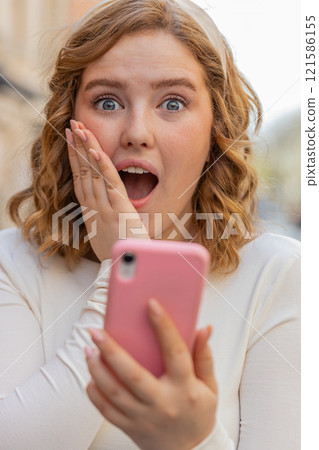 Excited happy winner young woman use smartphone celebrating win good message news in city street 121586155