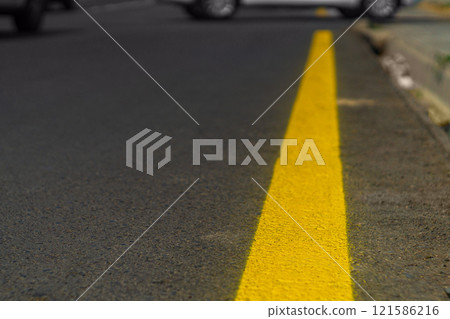 A section of the edge of an asphalt road with yellow solid road markings, taken from a low angle. In the background are the blurred wheels of cars driving out. Concept of intersecting paths ahead 121586216