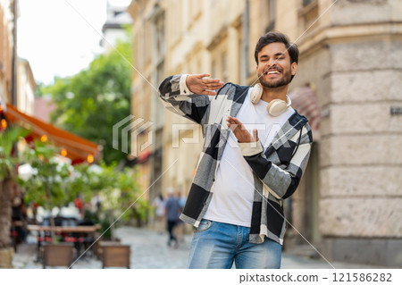 Cheerful rich Indian man showing wasting throwing money around hand gesture standing on city street 121586282
