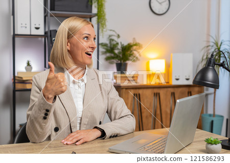 Happy mature Caucasian businesswoman freelancer in formal suit showing thumb up at home office desk Happy mature Caucasian businesswoman freelancer in formal suit showing thumb up at home office desk 121586293