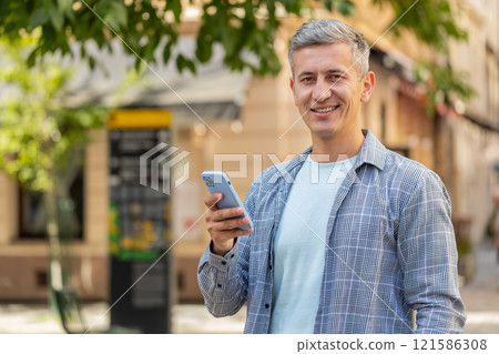 Smiling mature man using smartphone browsing internet, finishing work, looking at camera outdoors Smiling mature man using smartphone browsing internet, finishing work, looking at camera outdoors 121586308